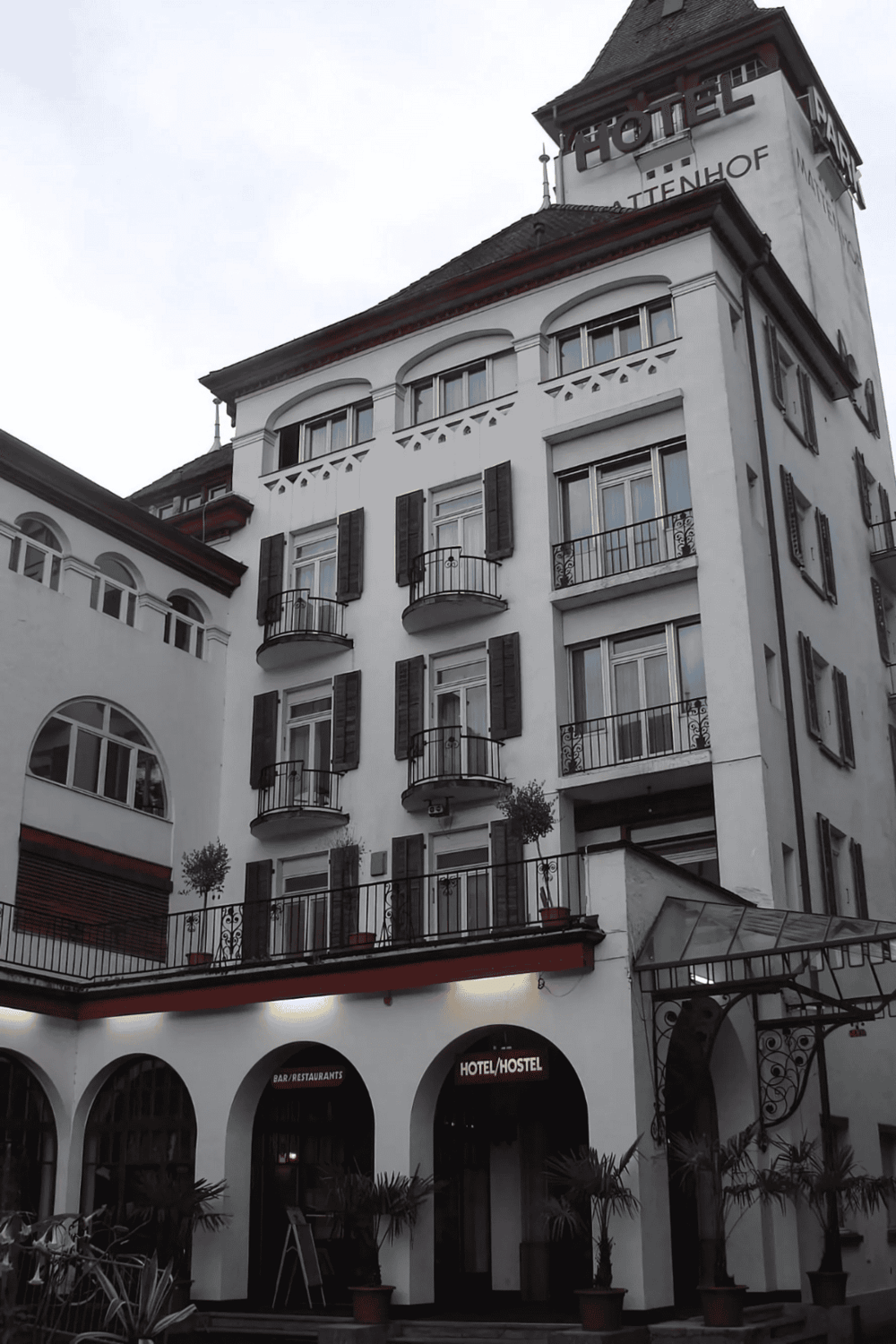 Elegant hotel building with balconies and black shutters, located in a bustling city area.