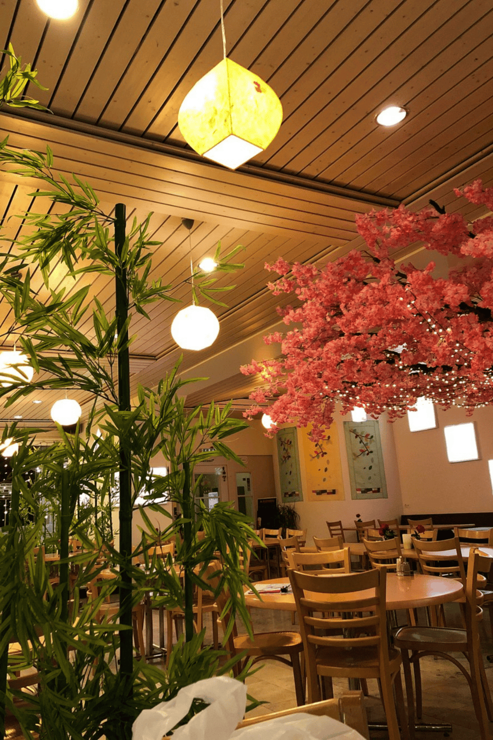 Cozy interior of a restaurant with wooden furniture, pink cherry blossom decor, and warm lighting.