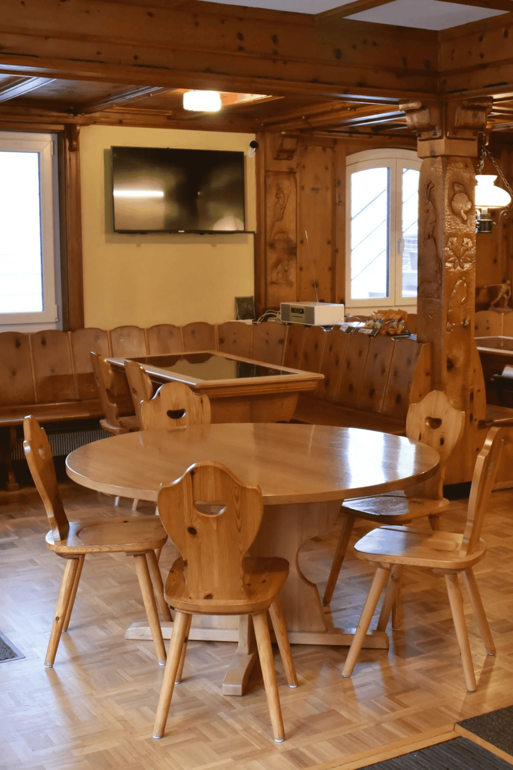 Cozy wooden dining area with rustic furniture and a wall-mounted TV in a warm, inviting setting.