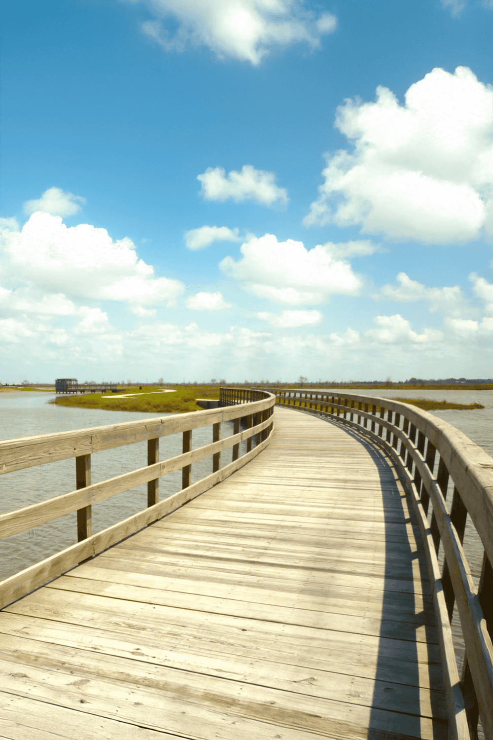 Wooden boardwalk over water with blue sky and clouds, scenic outdoor pathway | QuestForDirections.