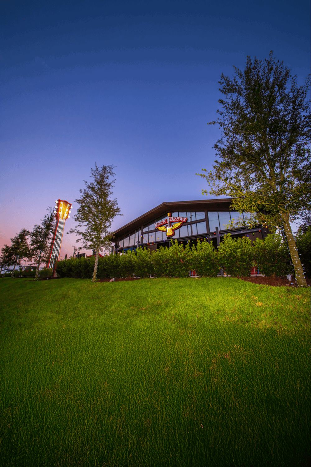 1. Modern brewery building with illuminated sign and guitar-themed towers at dusk.