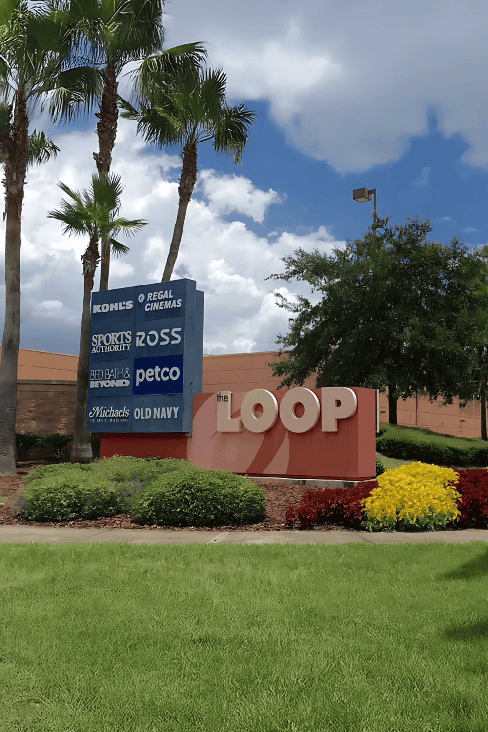 Vibrant shopping center entrance with palm trees, lush landscaping, and clear sky, anchored by The Loop shopping mall and retail stores.
