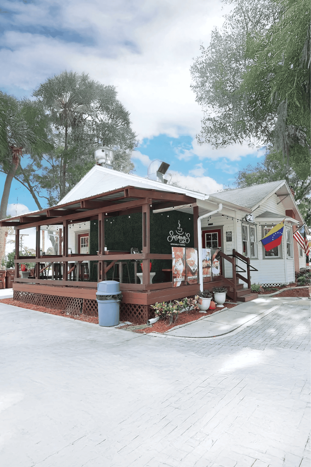 Cozy cafe with outdoor seating, flags, and lush trees in sunny weather, offering a welcoming atmosphere.