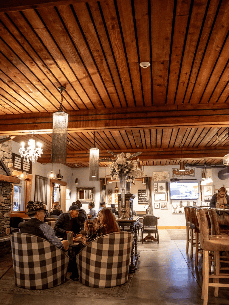 Cozy rustic restaurant interior with wooden ceiling, elegant lighting, and a group enjoying conversation.