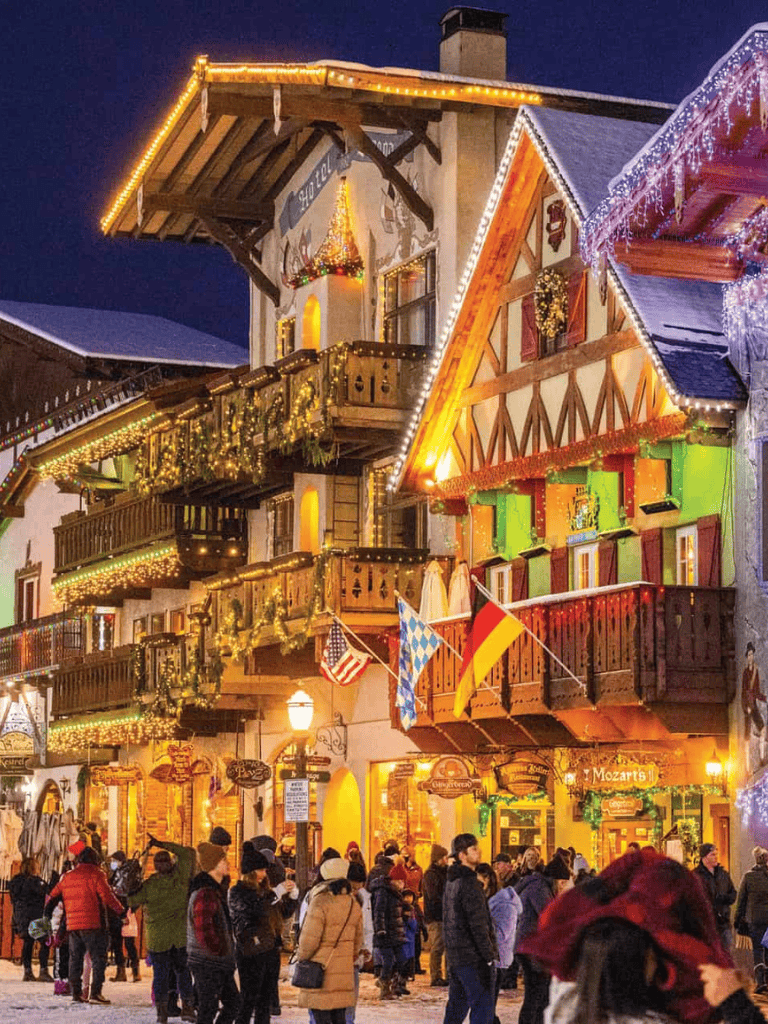 Festive Bavarian-style buildings illuminated with Christmas lights in a lively holiday market scene.