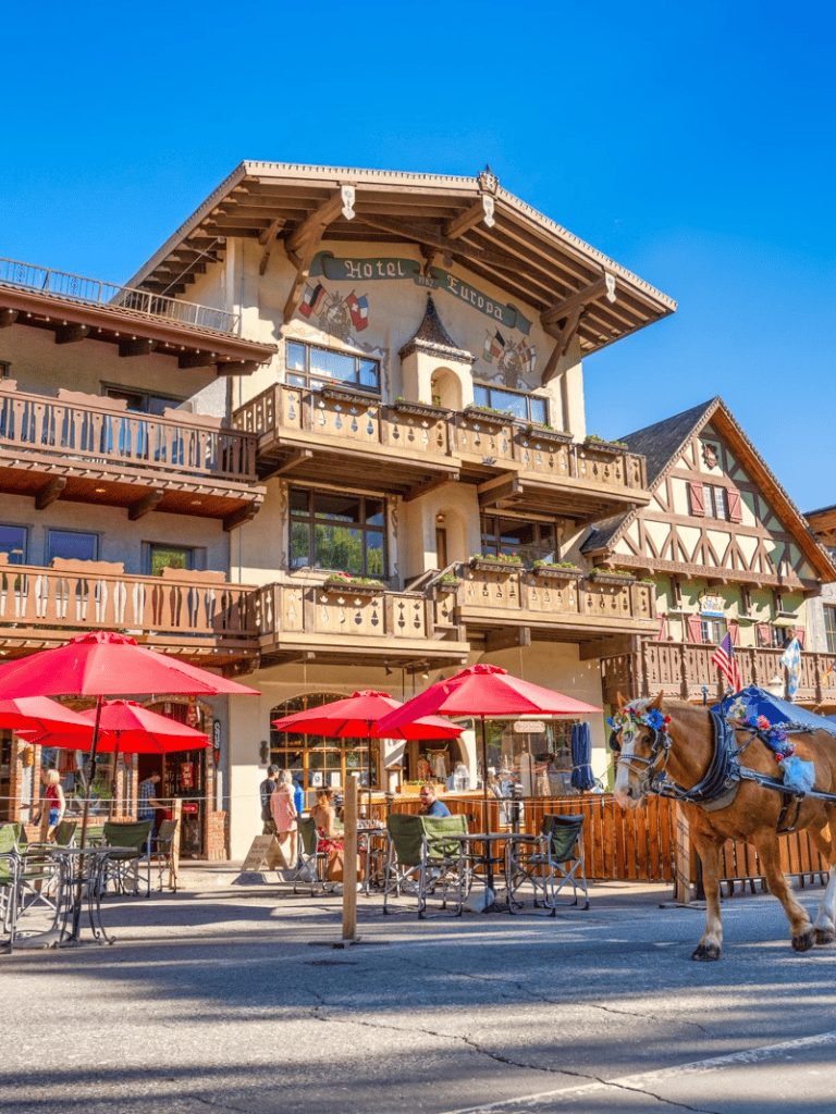 Charming Alpine hotel facade with outdoor seating and a decorated horse, reflecting European mountain village style.