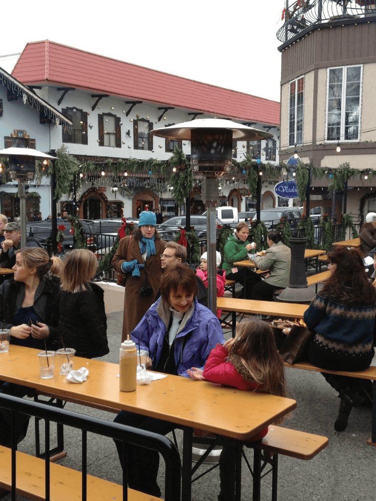 Enjoying outdoor dining at a festive holiday market with string lights and seasonal decorations.
