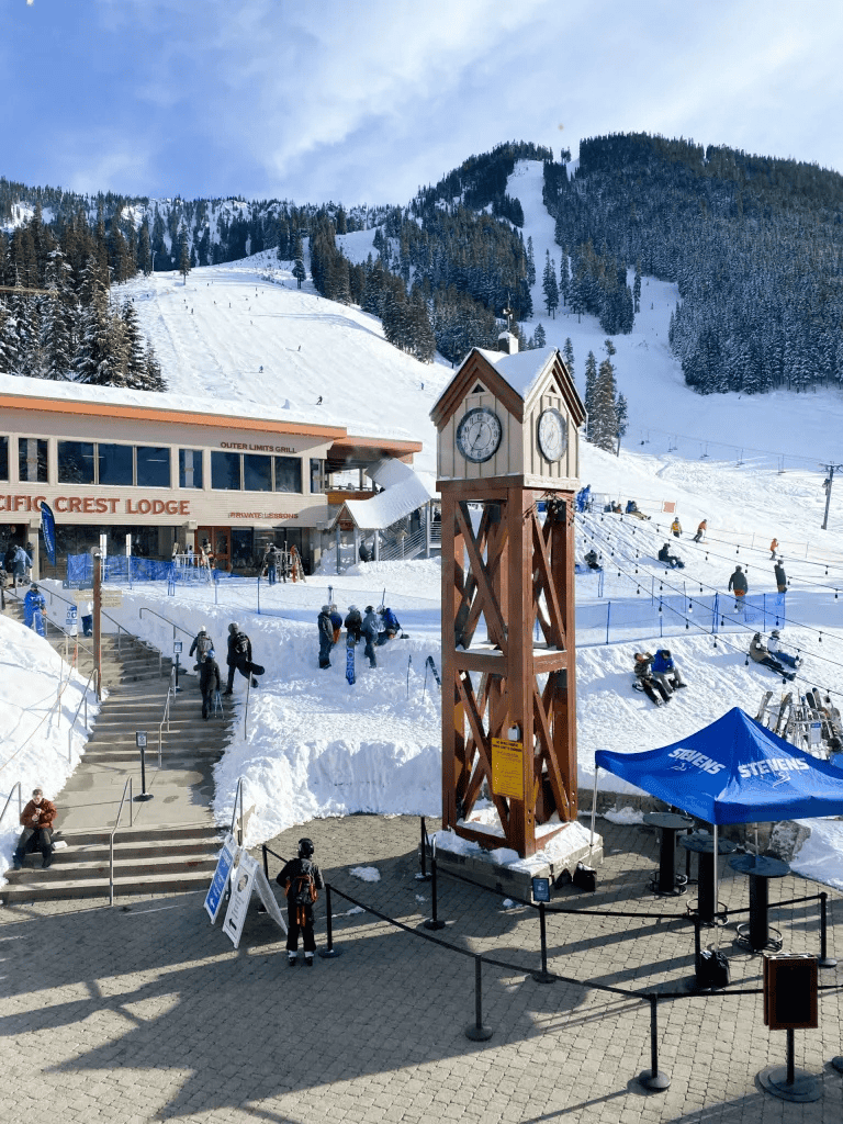 Snowy mountain resort with a clock tower, ski lifts, and visitors enjoying winter activities.