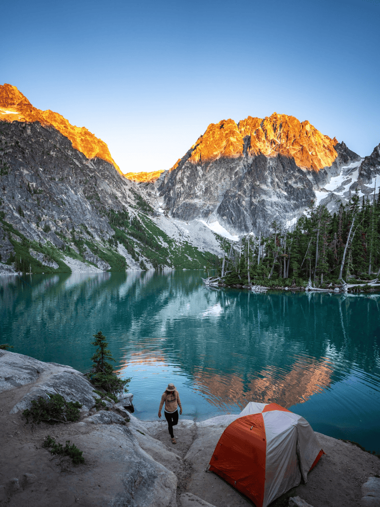 Serene mountain lake camping scene with tent and hiker, perfect for nature adventure enthusiasts.