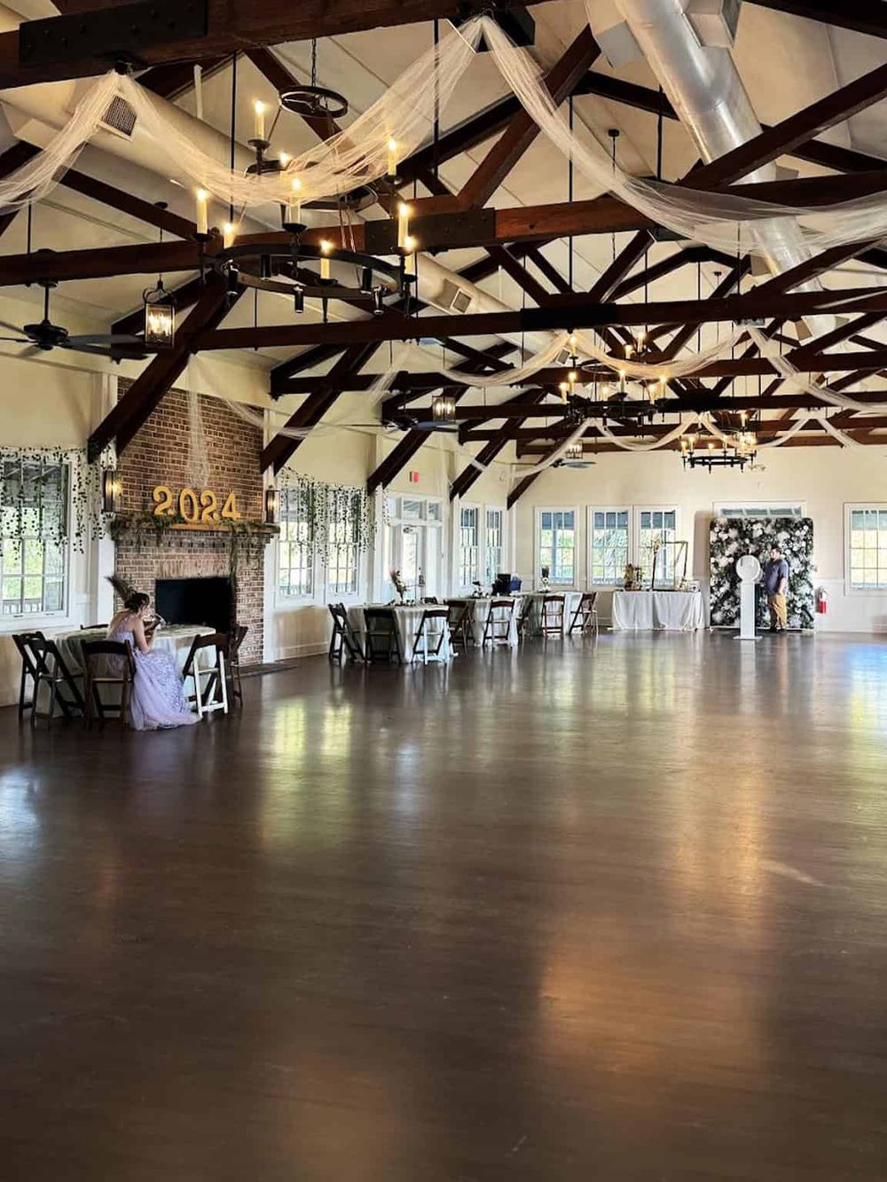 Spacious event hall with rustic wood beams, elegant lighting, and decorated for celebration or wedding. Perfect for memorable gatherings.