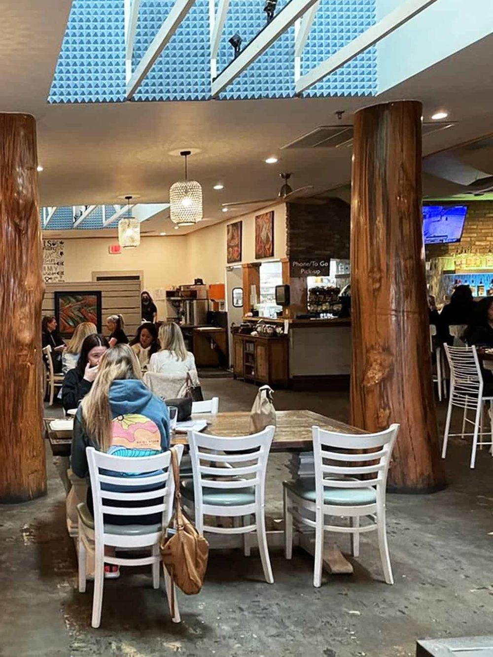 Cozy restaurant interior with wooden pillars, modern lighting, and patrons enjoying their meal in a warm, inviting atmosphere.