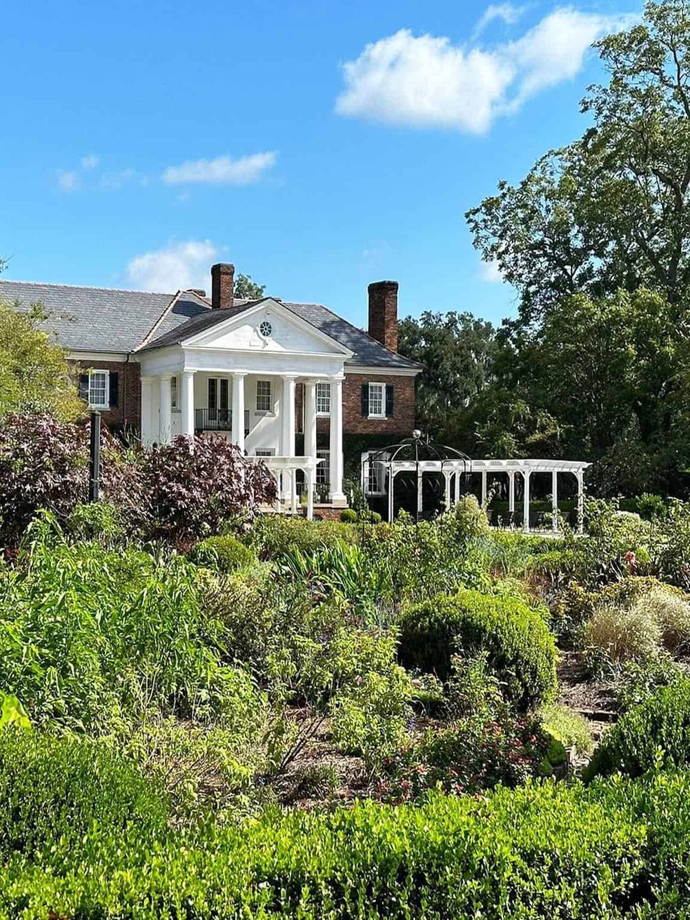 Elegant garden house with white columns and lush landscape, perfect for outdoor events or relaxing retreats.