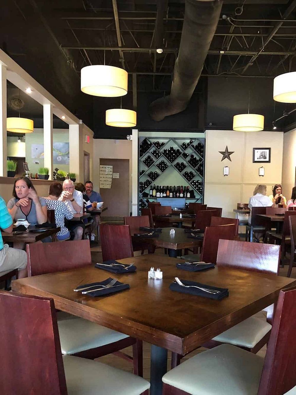 Cozy restaurant interior with wooden tables, wine display, and soft lighting, ideal for dining and socializing.