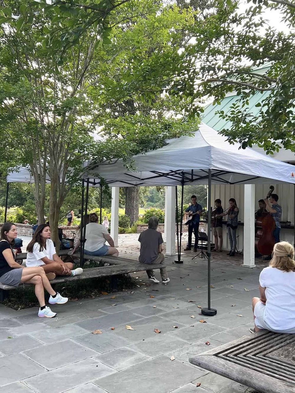 Live outdoor music performance at Quest for Directions park, featuring a band under a tent with audience enjoying the show.