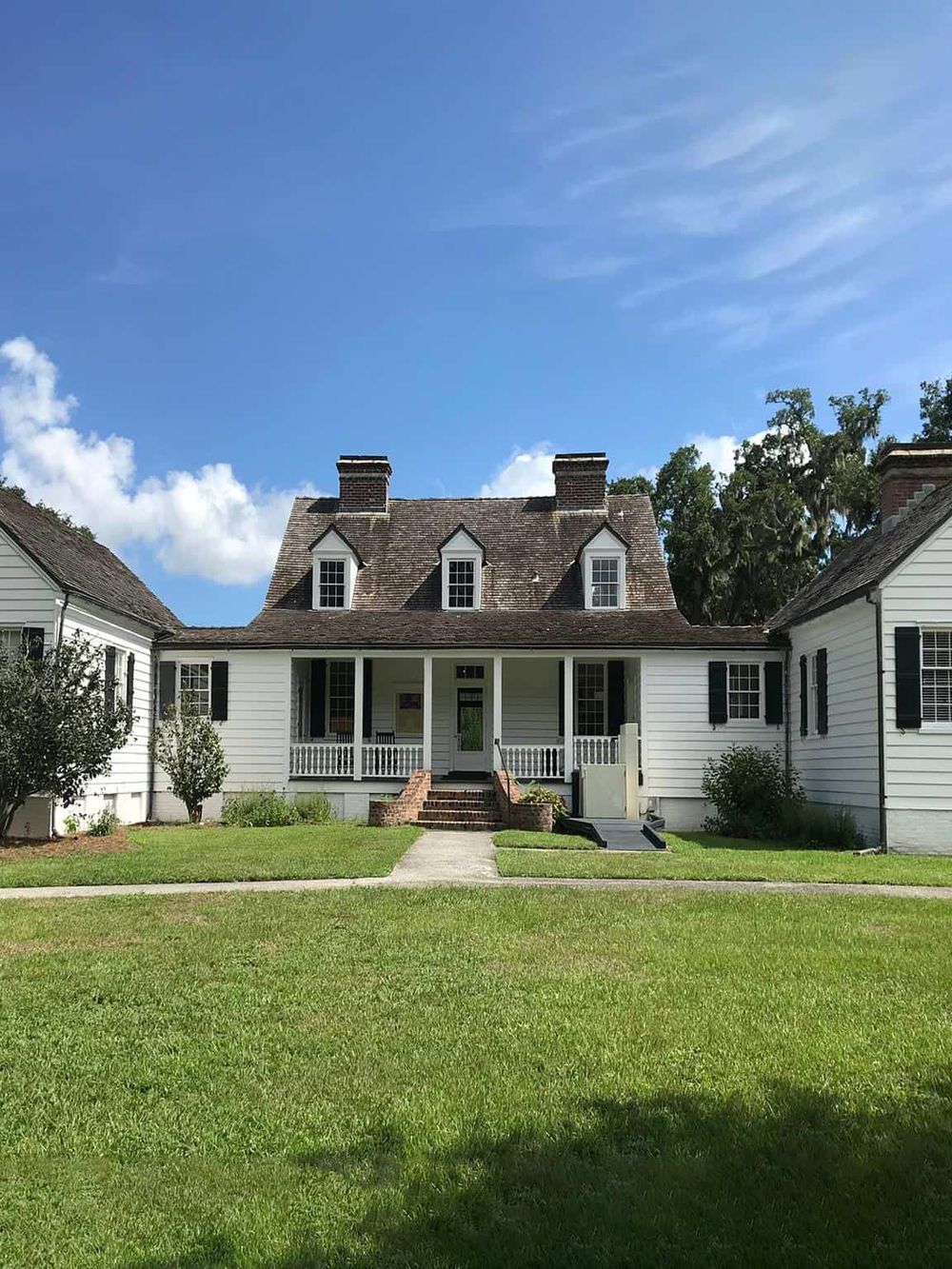 Charming white historic house with front porch, set against a clear blue sky and lush greenery.