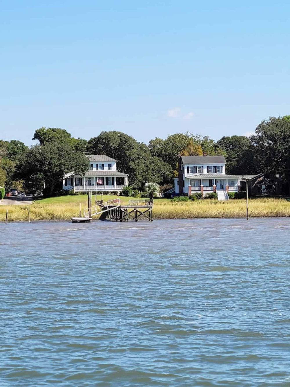 Waterfront houses on a serene riverbank with lush trees and a clear blue sky, perfect for scenic travel destinations.