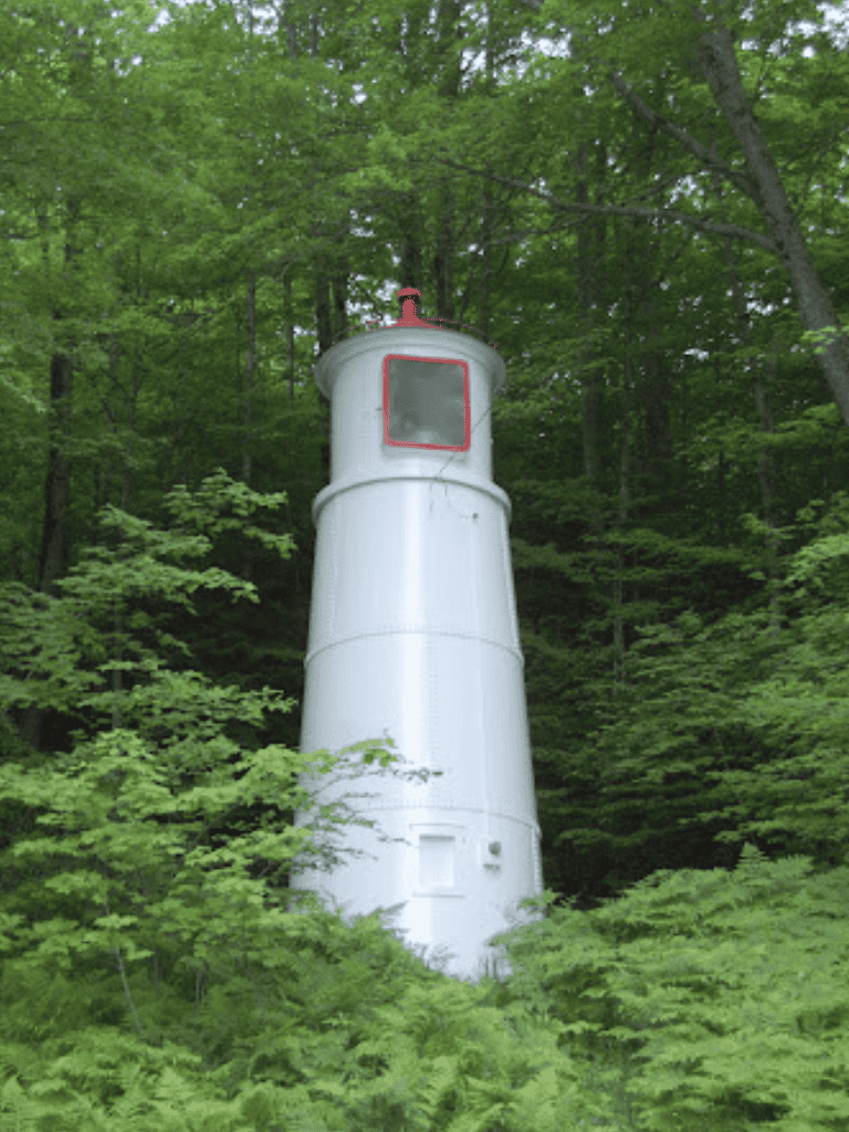 Rustic lighthouse surrounded by lush green forest in scenic outdoor setting.