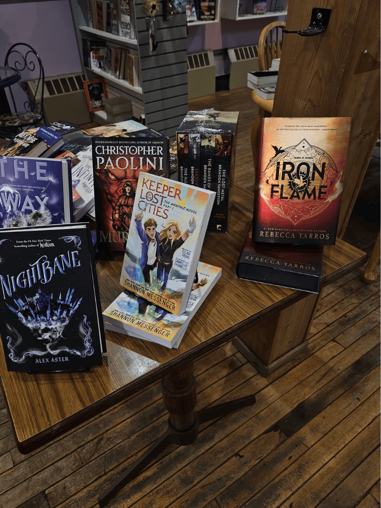 Fantasy book display at QuestForDirections bookstore, featuring titles like Iron Flame and Keeper of Lost Cities.