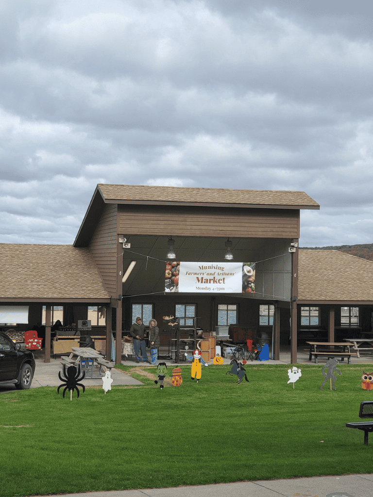 Farmers market with festive Halloween decorations and outdoor seating, promoting local produce and artisan goods.