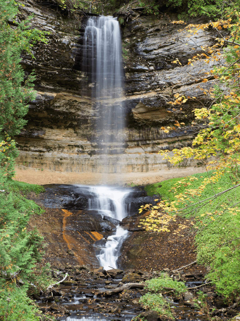 Serene waterfall cascading over rocky cliffs surrounded by lush greenery in fall.