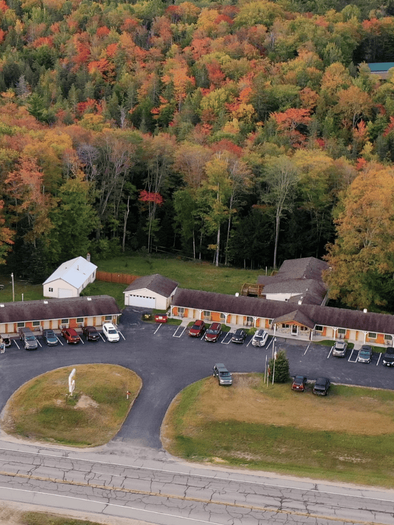 Aerial view of a motel surrounded by colorful fall trees and a parking lot with several cars.