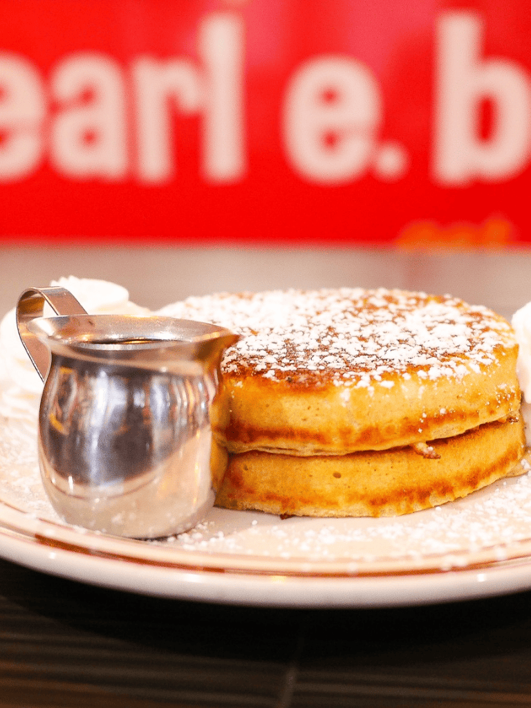 Golden pancakes with powdered sugar and syrup on a white plate, breakfast food, home cooking, tasty and inviting.