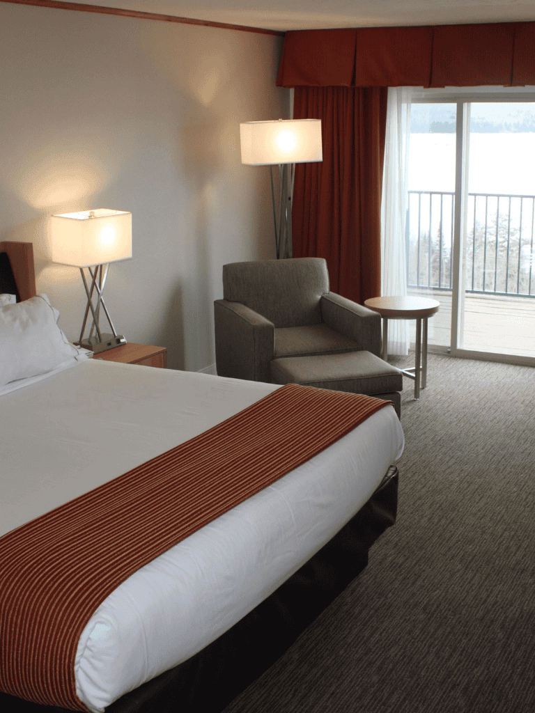 Cozy hotel bedroom with comfortable bed, armchair, and balcony overlooking scenic views, perfect for relaxing stays.