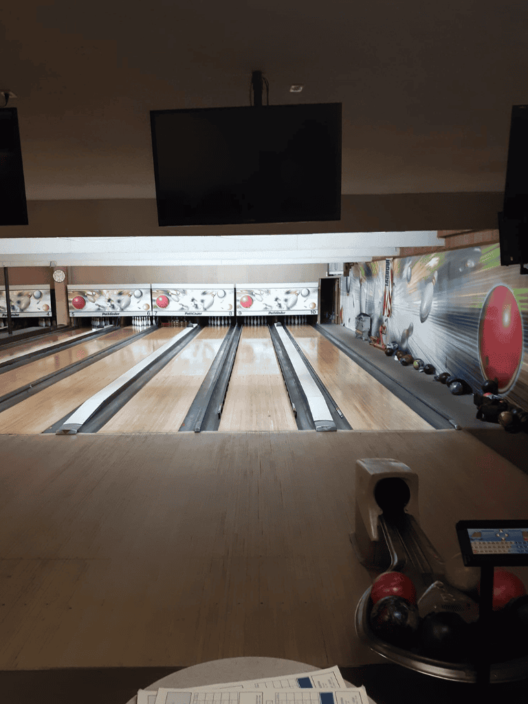 Bright modern bowling alley with multiple lanes and large screens for entertainment and scoring.