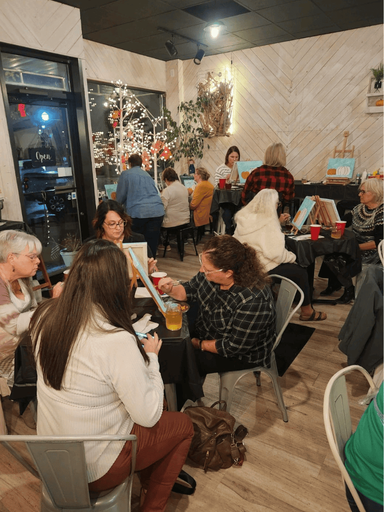People participating in an art class at QuestForDirections studio, creating holiday-themed paintings in a cozy, festive atmosphere.