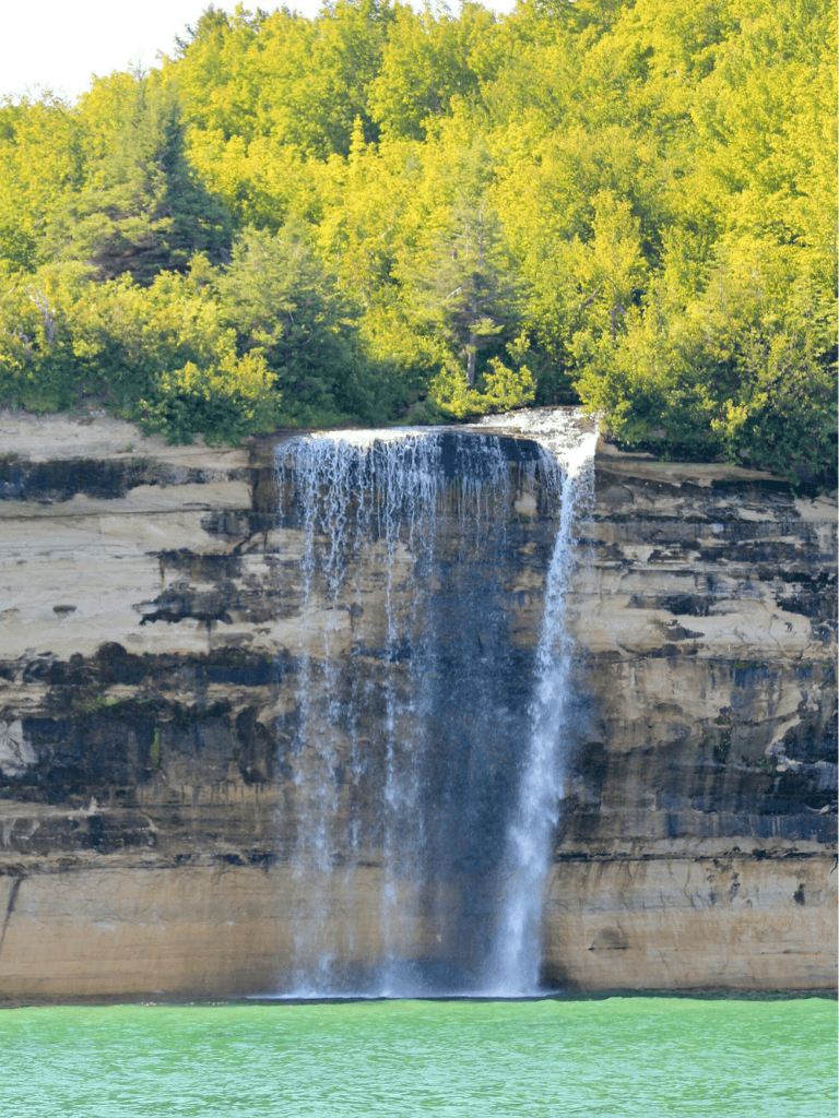 Tranquil waterfall flowing into a lush green river with vibrant trees in the background.