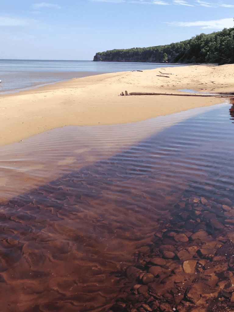 Calm beach with clear water and lush green cliffs in background.