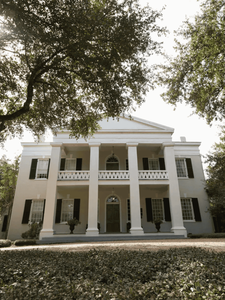 Elegant white mansion with grand columns and lush surroundings.