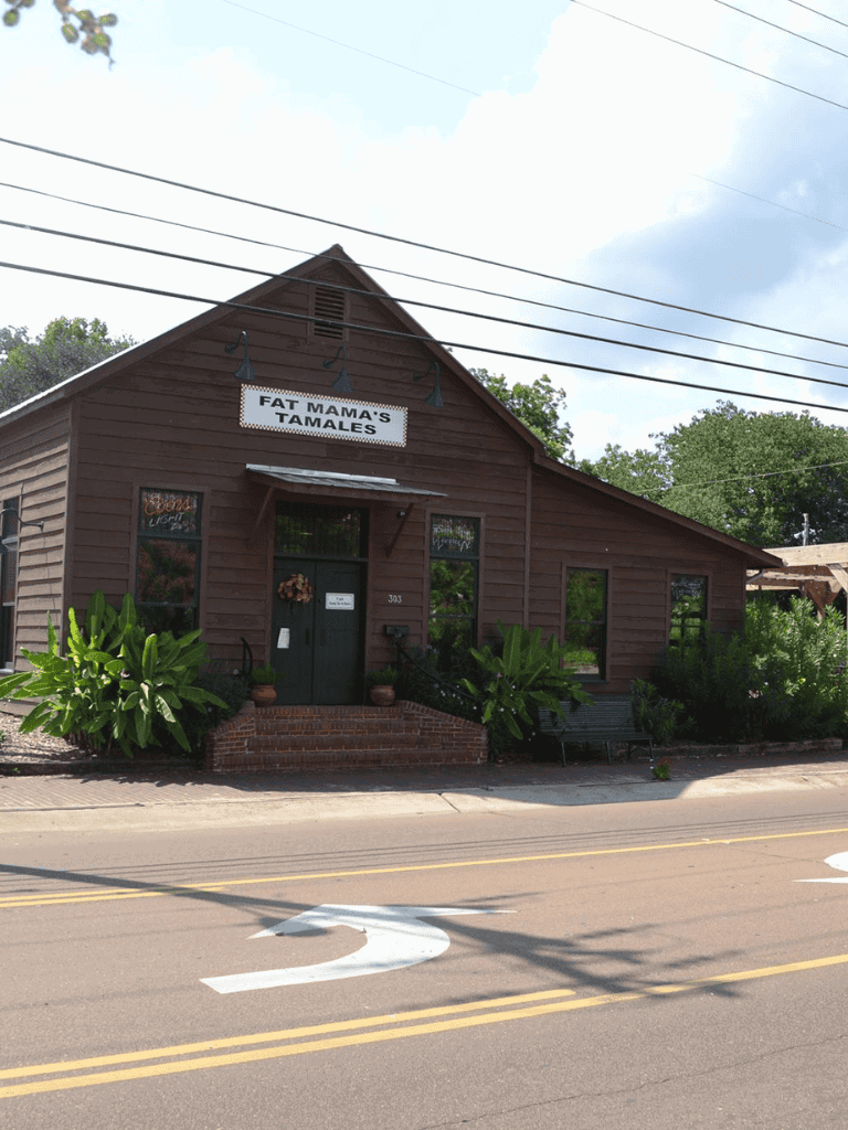 Cozy restaurant, Fat Mama's Tamales, on a quiet street with lush greenery and vibrant plants outside.