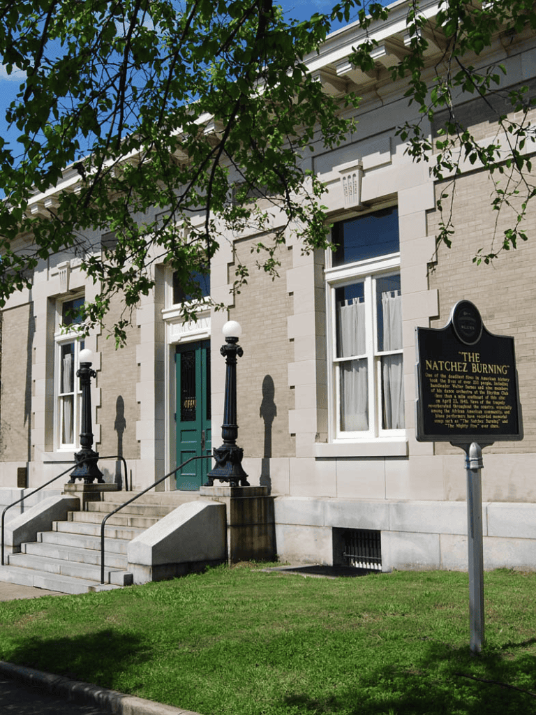 Historic building with sign marking The Natchez Burning, Barker and Quest for Directions in the background.