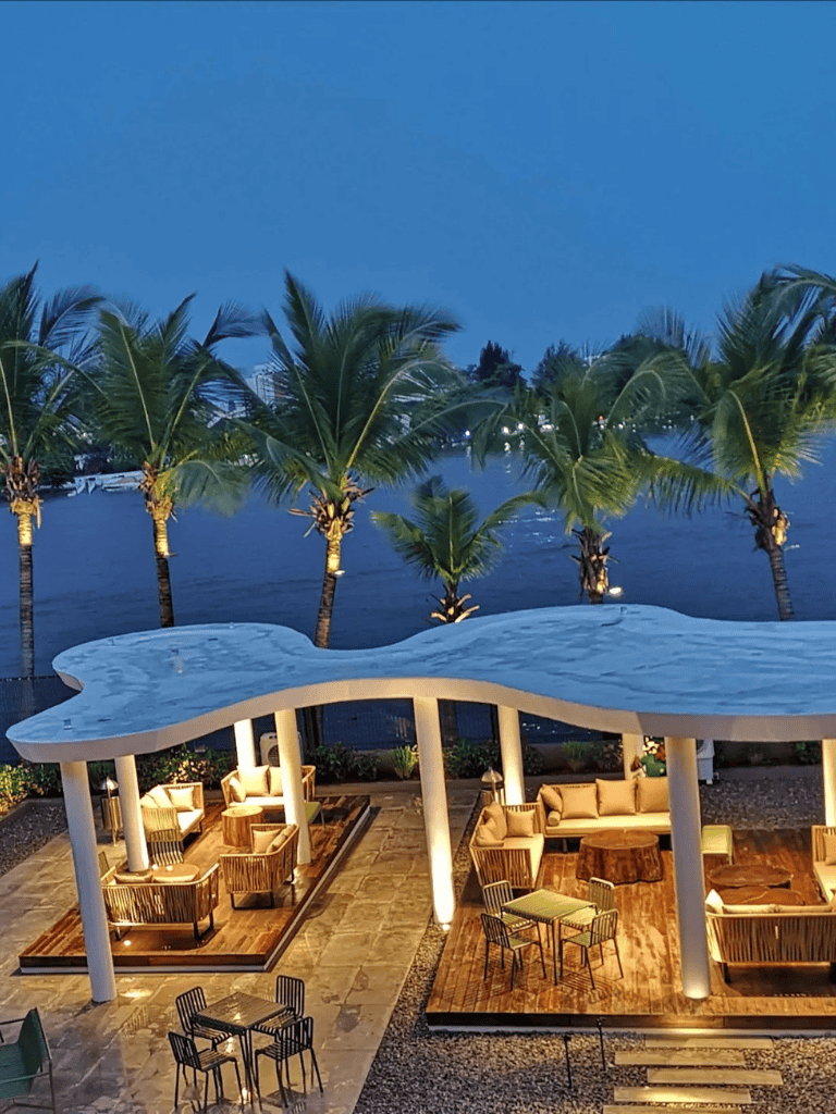 Luxurious waterfront outdoor lounge area with tropical palm trees and scenic river view at dusk.