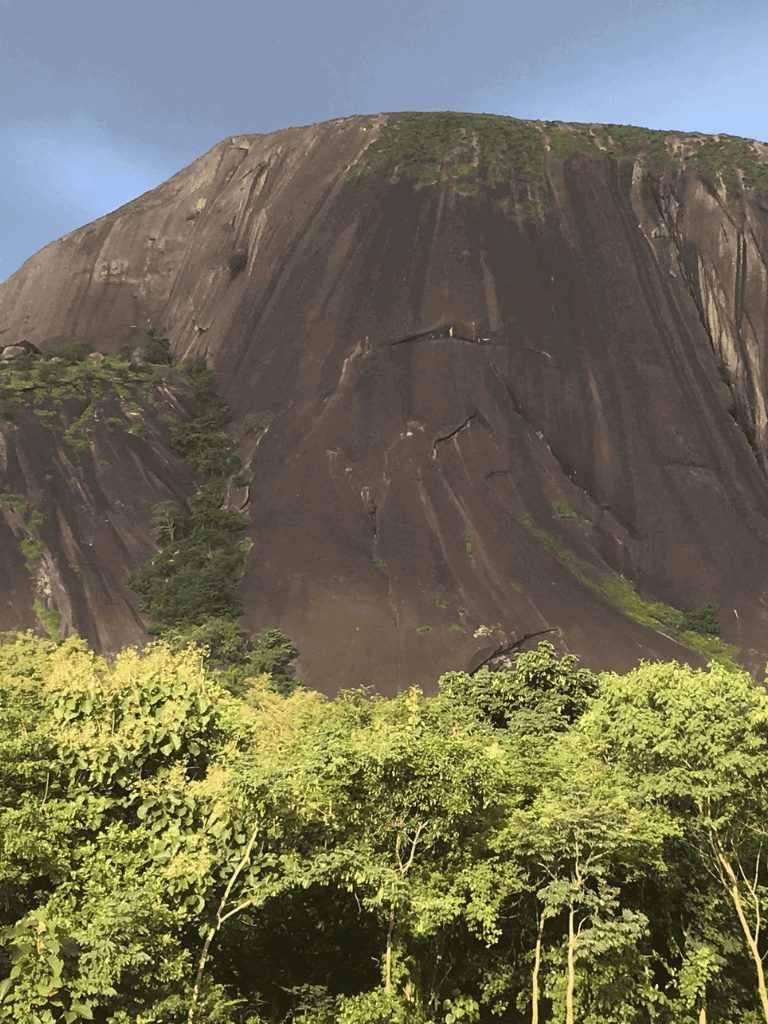 Vast granite mountain with lush green forest at base, scenic outdoor adventure location.