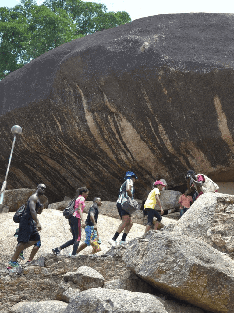 Climbing large boulder at Quest for Directions adventure site in Kenya.