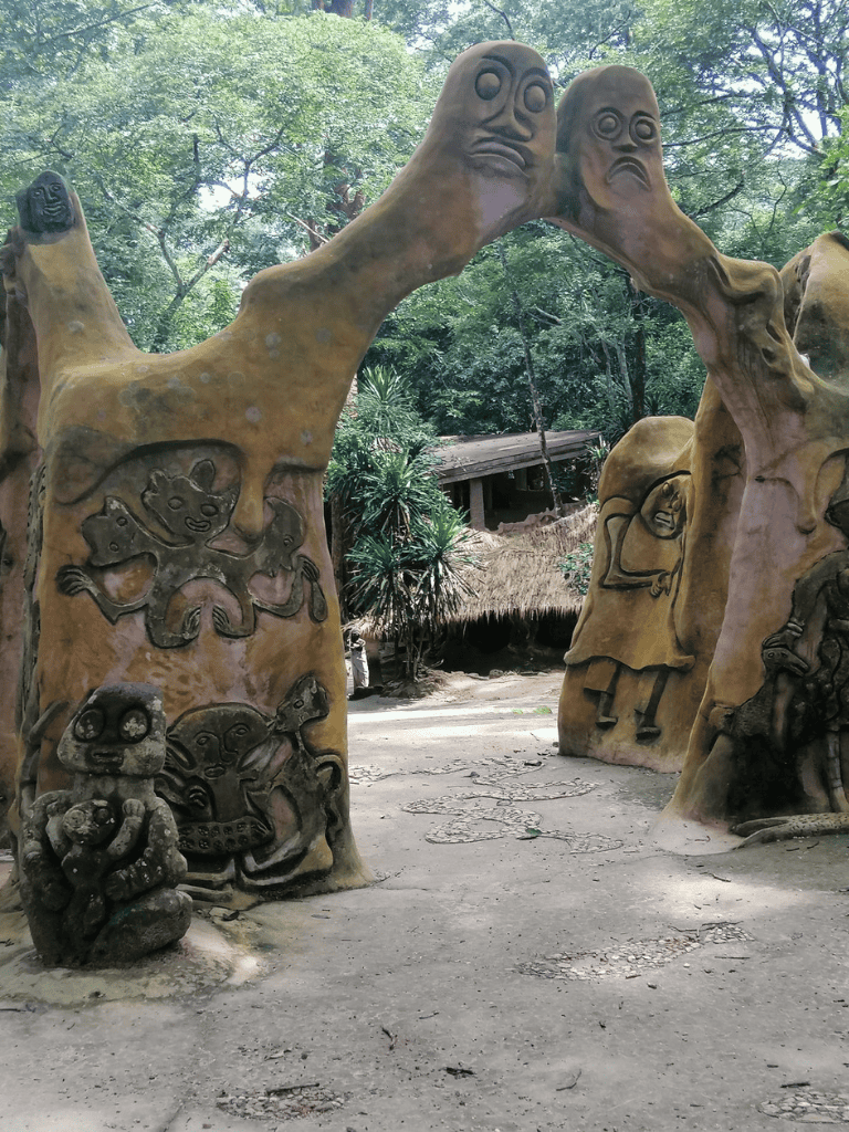 Colorful tribal art sculpture with faces and animals in a lush forest setting.