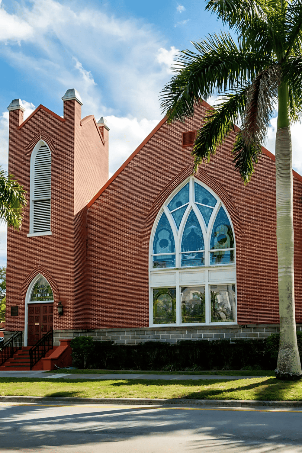 Historic red brick church with stained glass windows and palm trees, located in sunny Florida.