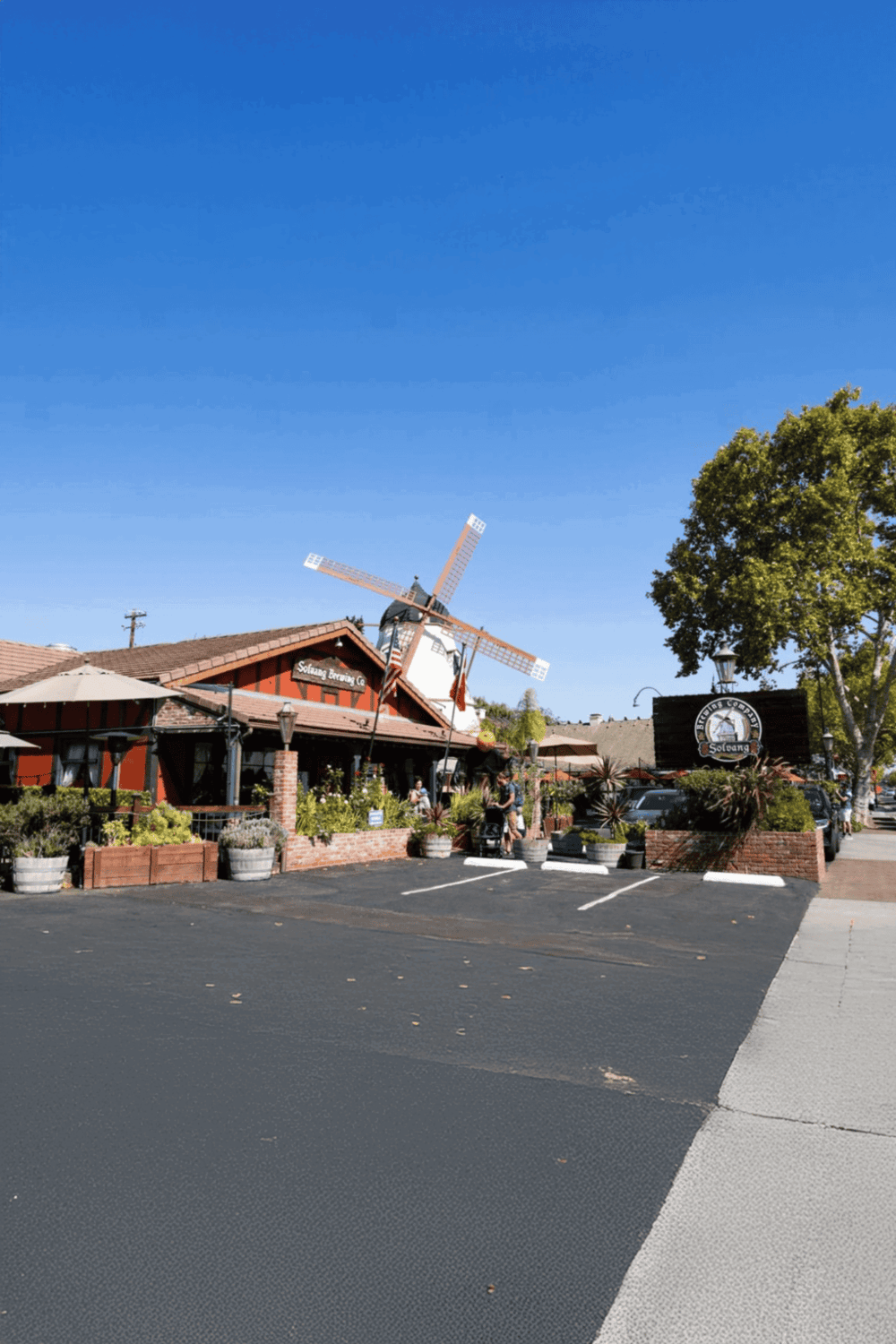 Charming brewery restaurant with outdoor seating and a decorative windmill under a clear blue sky.