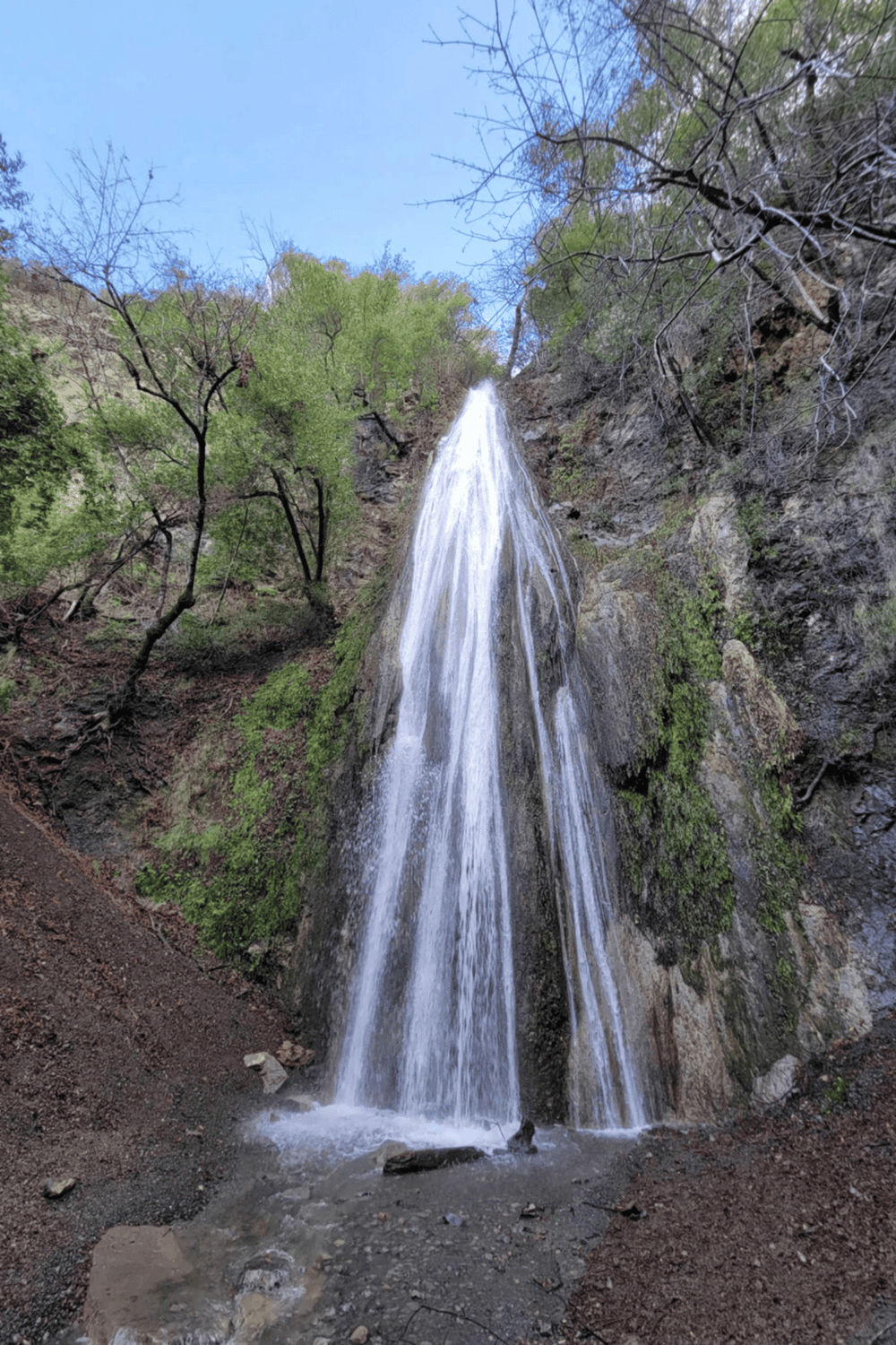 Waterfall in scenic natural setting with lush green trees and rocky terrain.