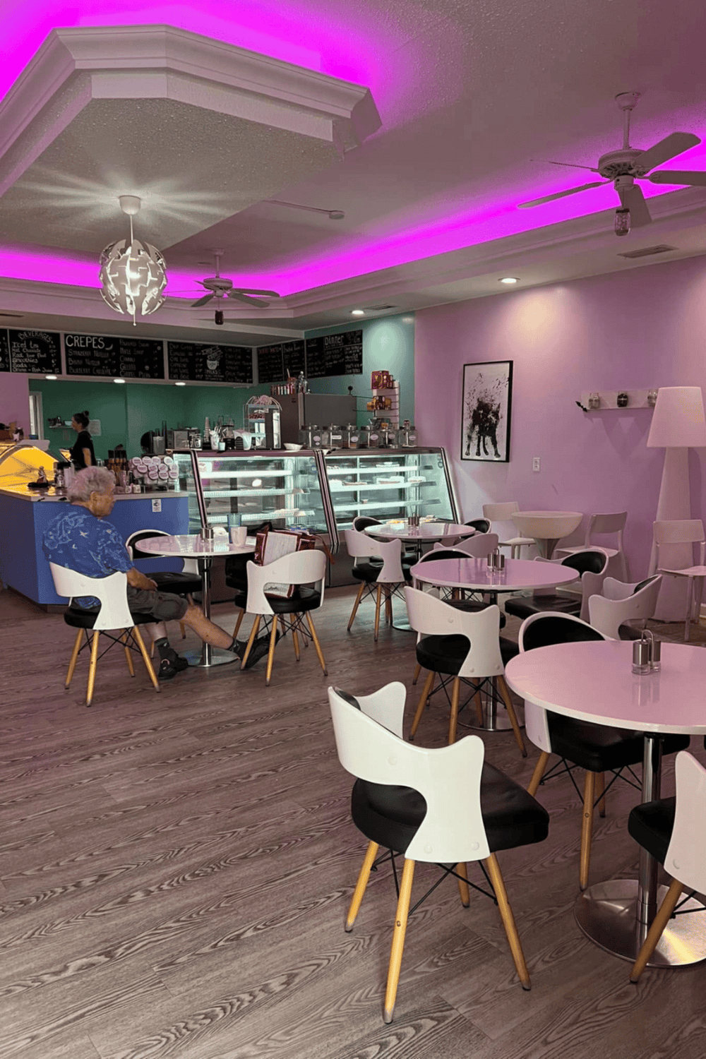 Bright pastel-colored café interior with neon pink lighting, modern tables, and a glass dessert display case.