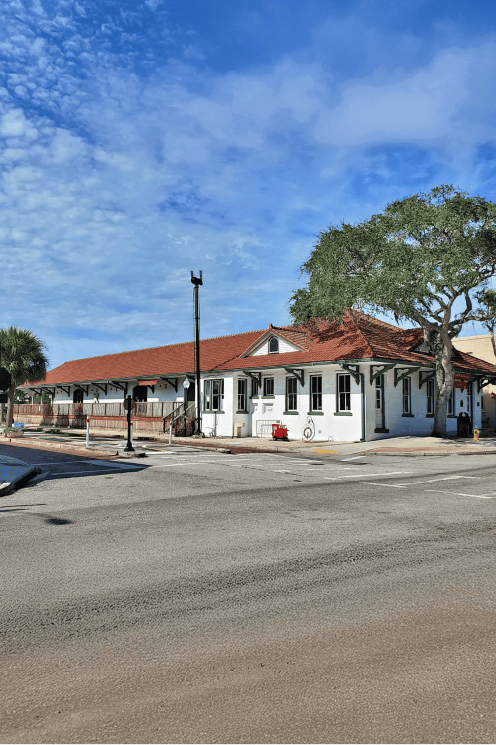 Vintage train station with red-tiled roof and surrounding trees, located in a historic downtown area.