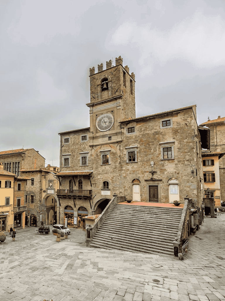 Ancient stone clock tower building in a historic town square in Italy.