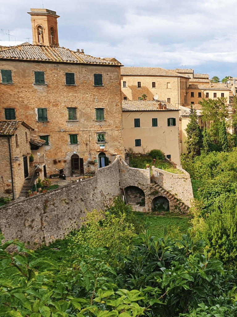 Ancient Tuscan village walls with historic buildings and lush greenery in Italy.