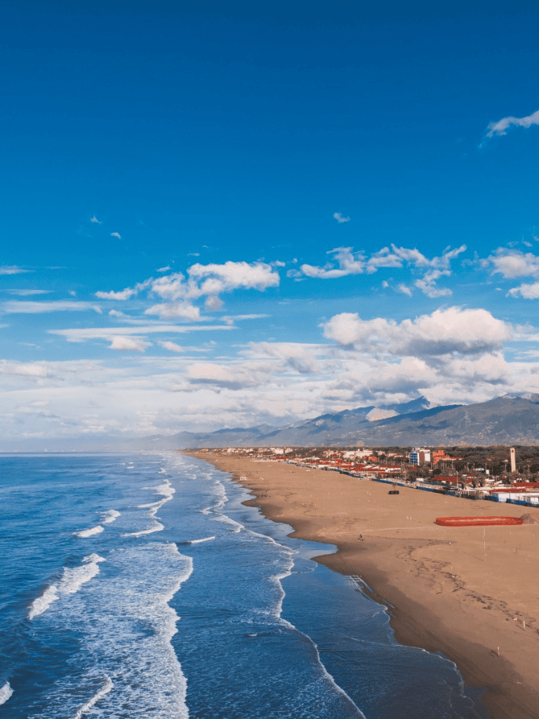 Beautiful coastal beach with mountains in the background and clear blue sky, perfect for travel and outdoor adventures.