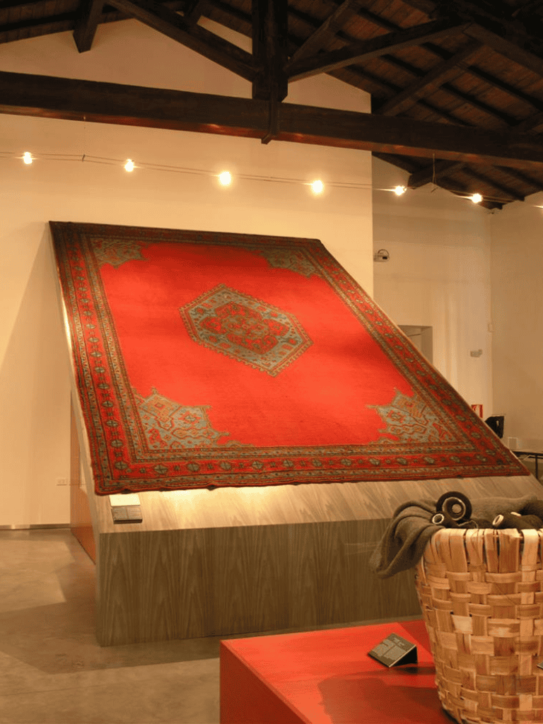 Vintage red rug displayed on a raised platform at QuestForDirections exhibit.