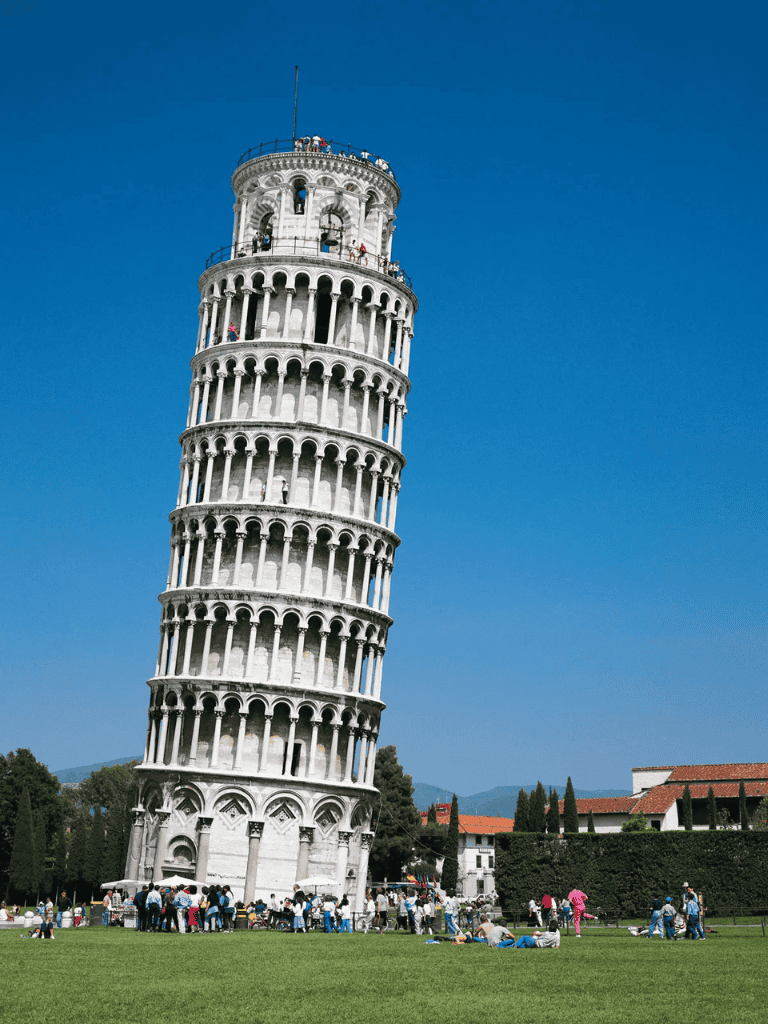Ancient Leaning Tower of Pisa with tourists, blue sky, and green grass.