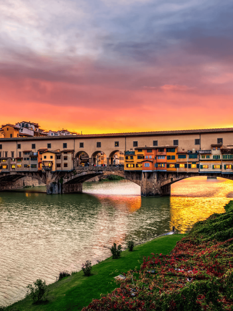 Colorful sunset over historic Ponte Vecchio in Florence, Italy, with vibrant sky and charming river views.
