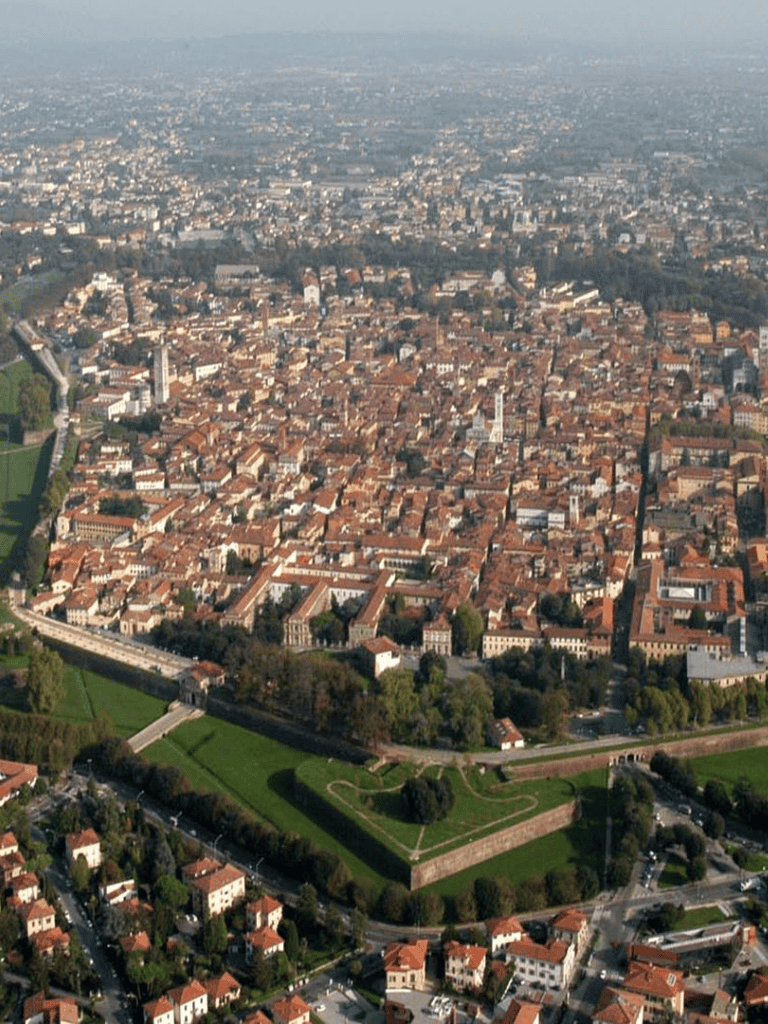 Aerial view of historic city with ancient structures and city walls, showcasing urban exploration in Italy.